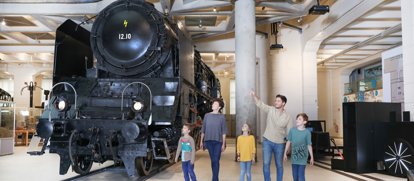 Eine Familie sieht sich gemeinsam die 12.10er Dampflokomotive an. In der Ausstellung "12.10 eine Dampflokomotive der Superlative" : 