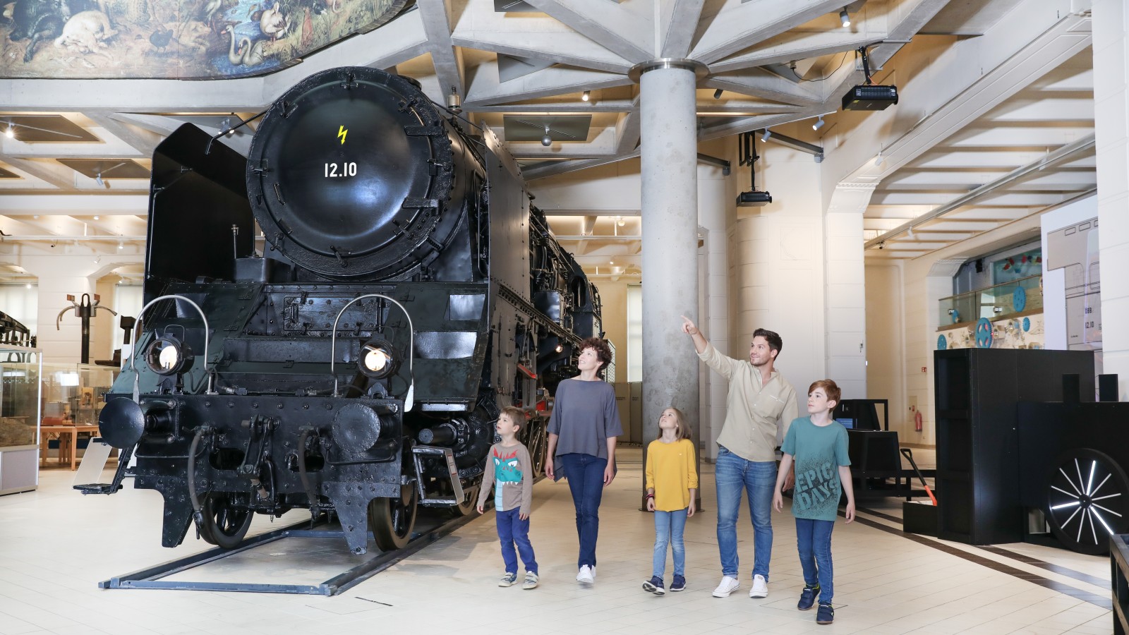 Eine Familie sieht sich gemeinsam die 12.10er Dampflokomotive an. In der Ausstellung "12.10 eine Dampflokomotive der Superlative" : 
